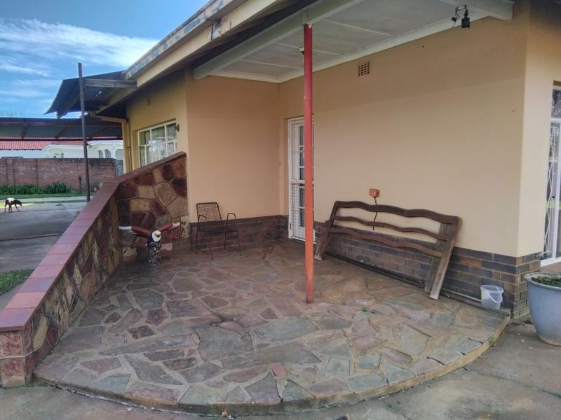 A covered patio area featuring stone paving and stone-clad retaining walls, providing a functional outdoor space with potential for cosmetic updates.