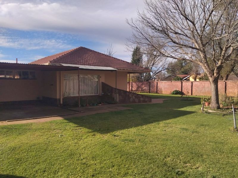 Rear view of the house featuring a tiled roof, covered patio area, stone cladding accents, and a spacious garden enclosed by a brick boundary wall.