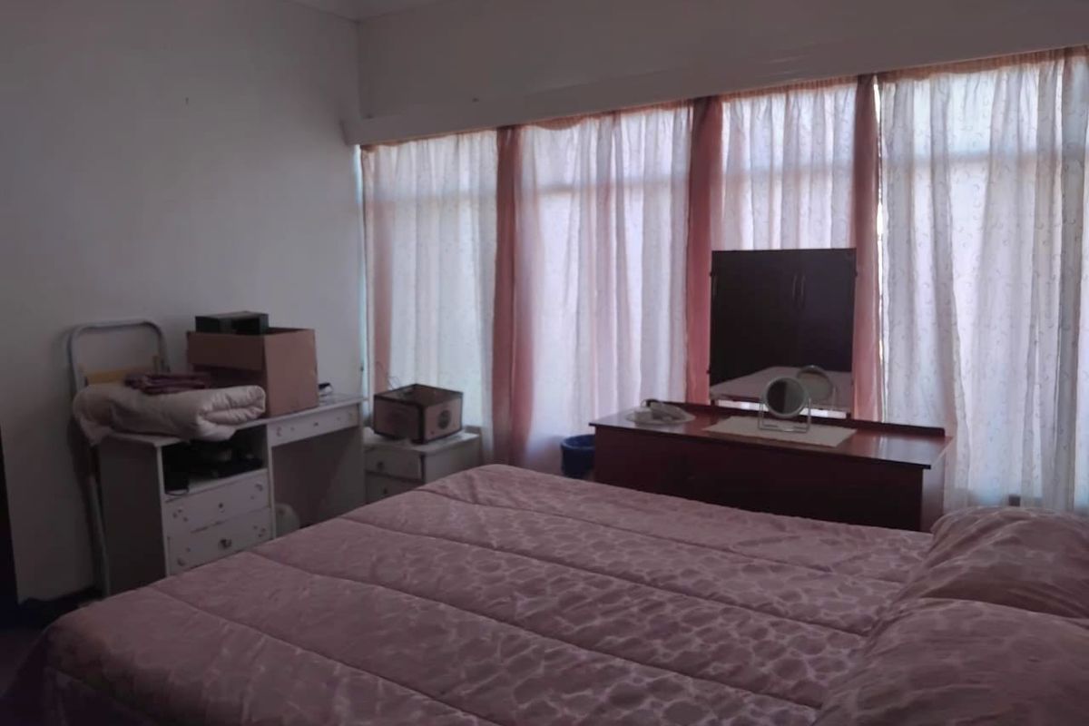 A bedroom featuring a large window with curtains, providing natural light. The space is functional with standard finishes.