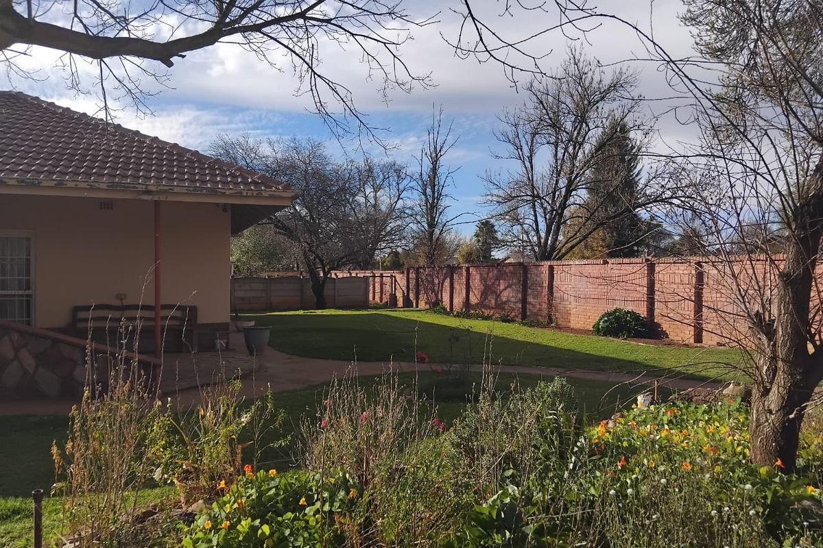 A spacious rear garden featuring a well-maintained lawn, paved pathways, and a secure brick boundary wall, viewed from the rear patio area.