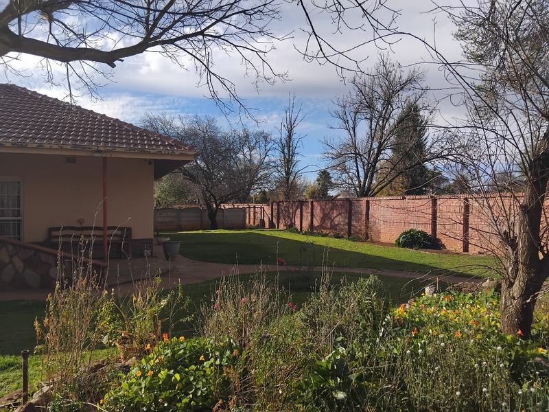 A spacious rear garden featuring a well-maintained lawn, paved pathways, and a secure brick boundary wall, viewed from the rear patio area.