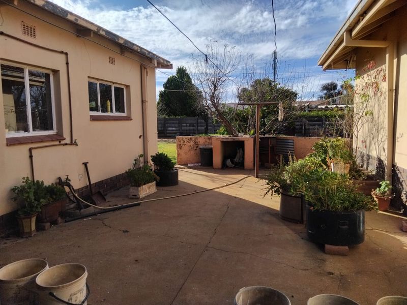 Rear courtyard area featuring a concrete patio, built-in braai, and perimeter walling, offering potential for outdoor entertainment space improvement.