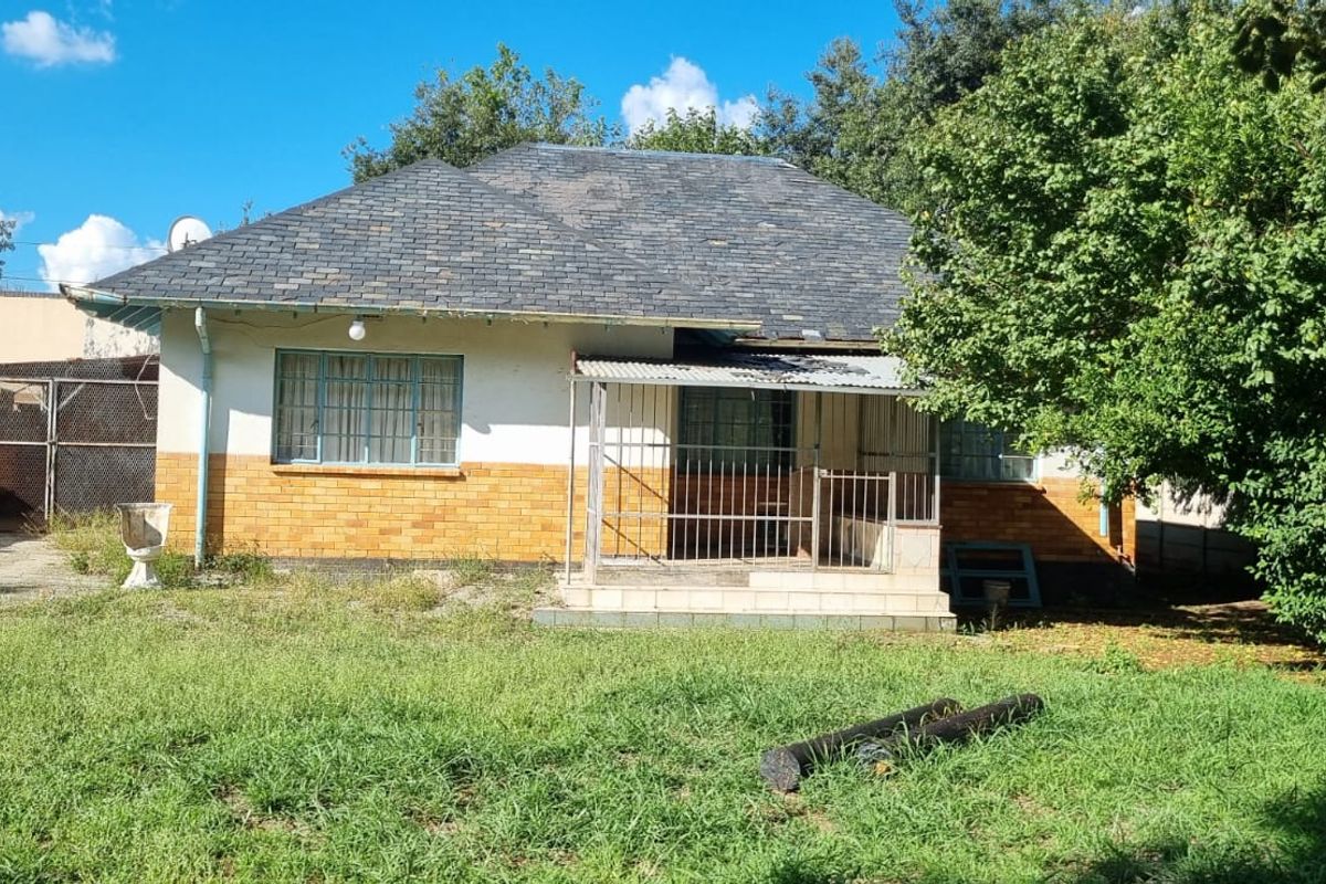 Rear view of a single-story house featuring a tiled roof, brick facade, and a covered porch area with security gates.