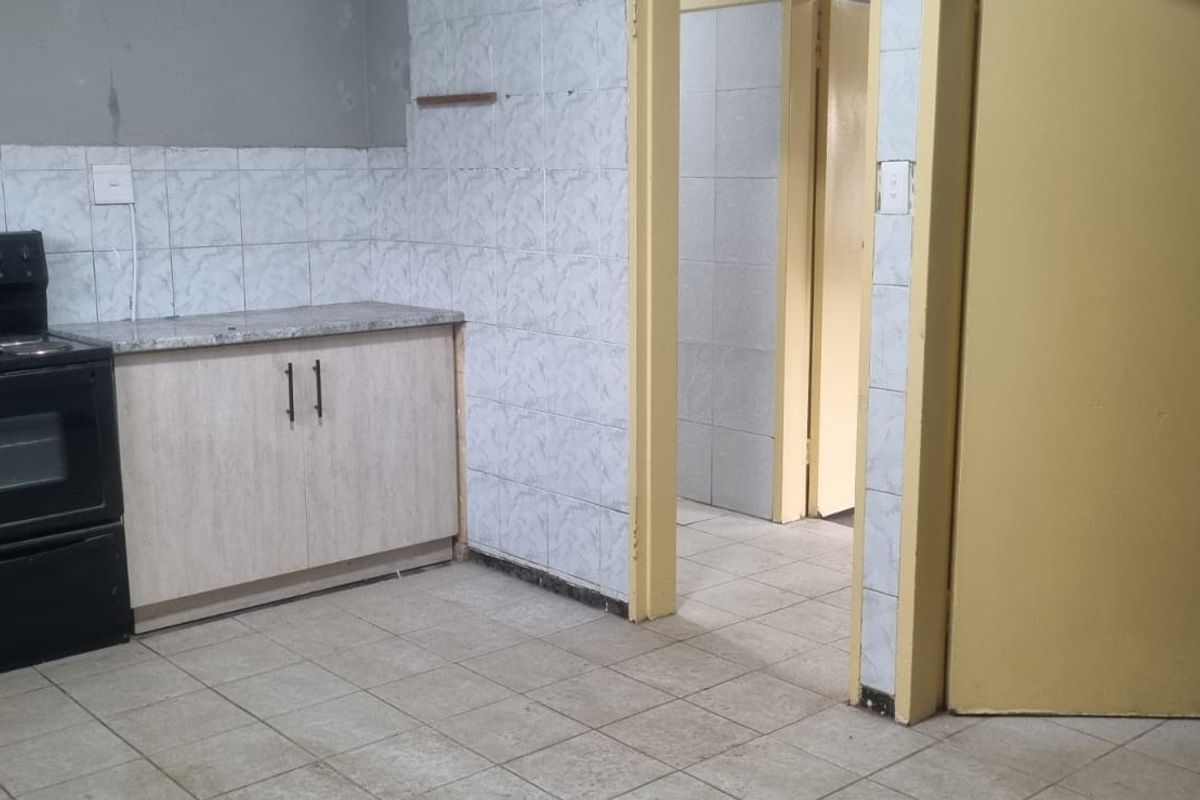 A functional kitchen space featuring tiled walls, laminate cabinetry, and a freestanding stove, requiring cosmetic updates to improve its overall condition and appeal.