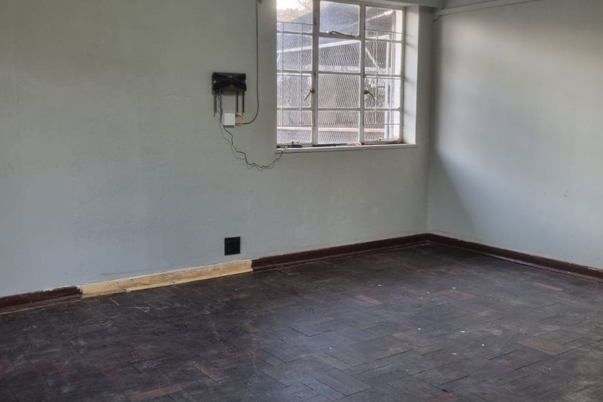 An empty bedroom featuring original parquet flooring and a steel-framed window, requiring cosmetic updates to restore its appeal.