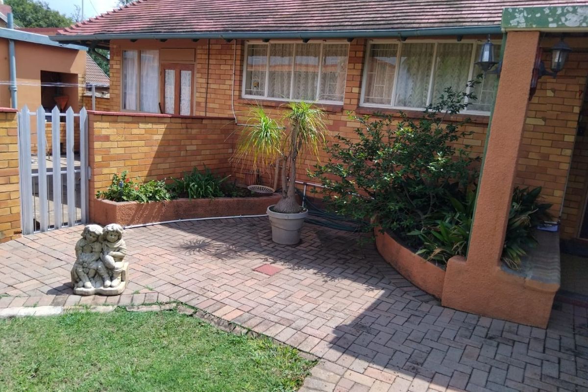 A rear exterior view of a brick house featuring a paved patio area, raised garden planters, and a tiled roof.