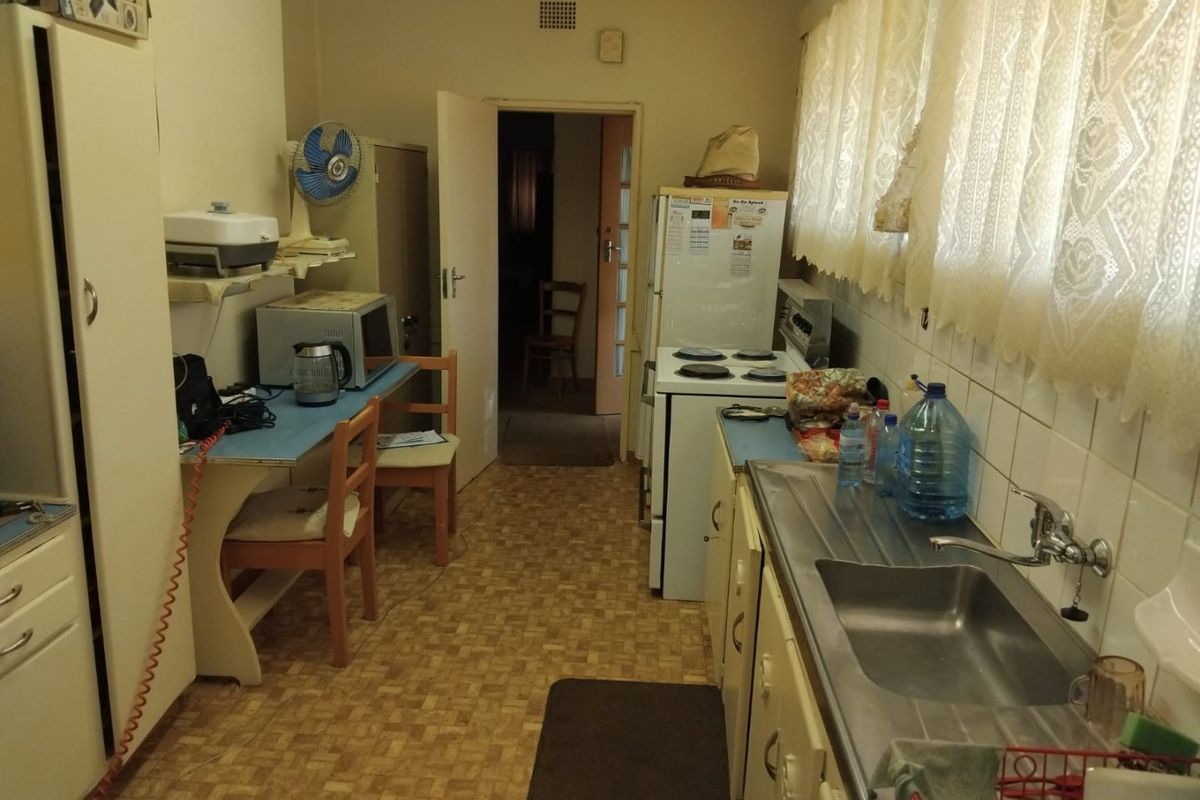 A dated kitchen featuring original cabinetry, a stainless steel sink, tiled splashback, and a freestanding electric stove with vinyl flooring.