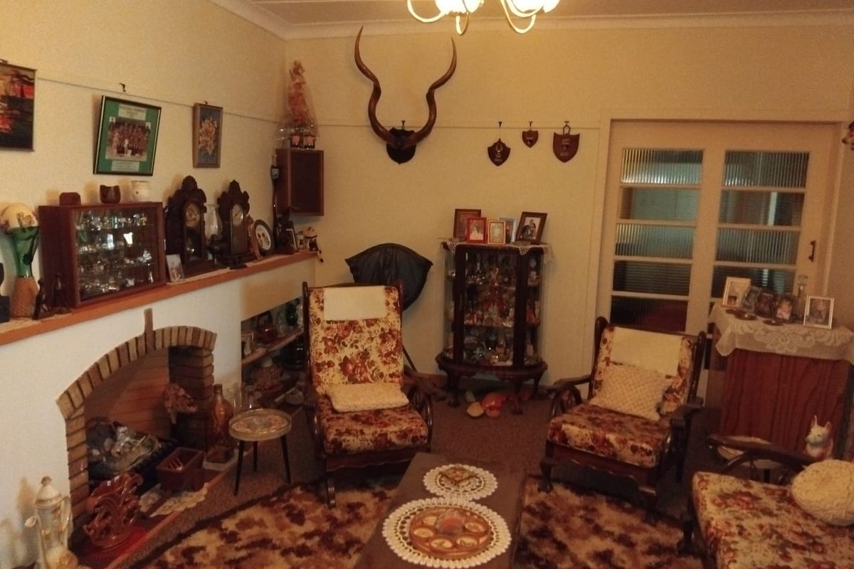 A traditional living room featuring a brick fireplace, coved ceiling, and glass-panelled internal door, offering a classic layout with potential for modernization.