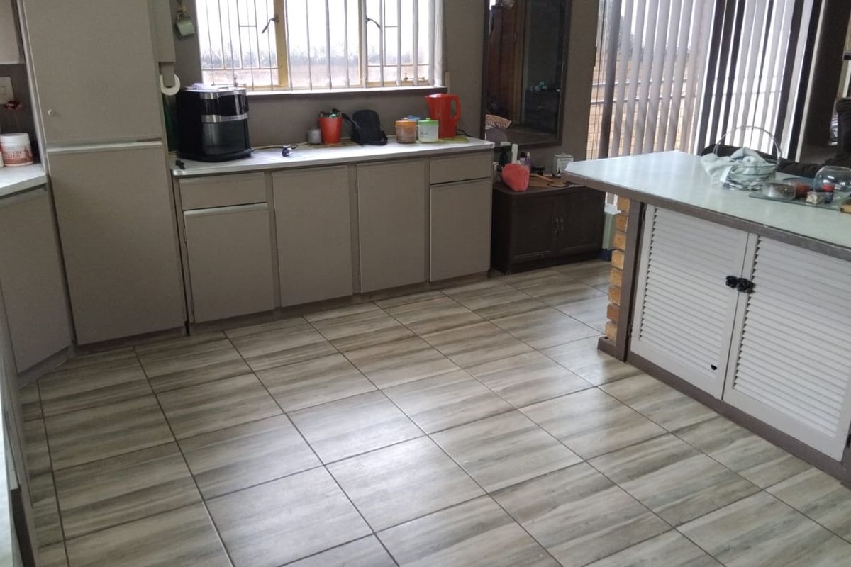 A functional kitchen area featuring built-in cabinetry, laminate countertops, a breakfast bar, and tiled flooring with security bars on the window.