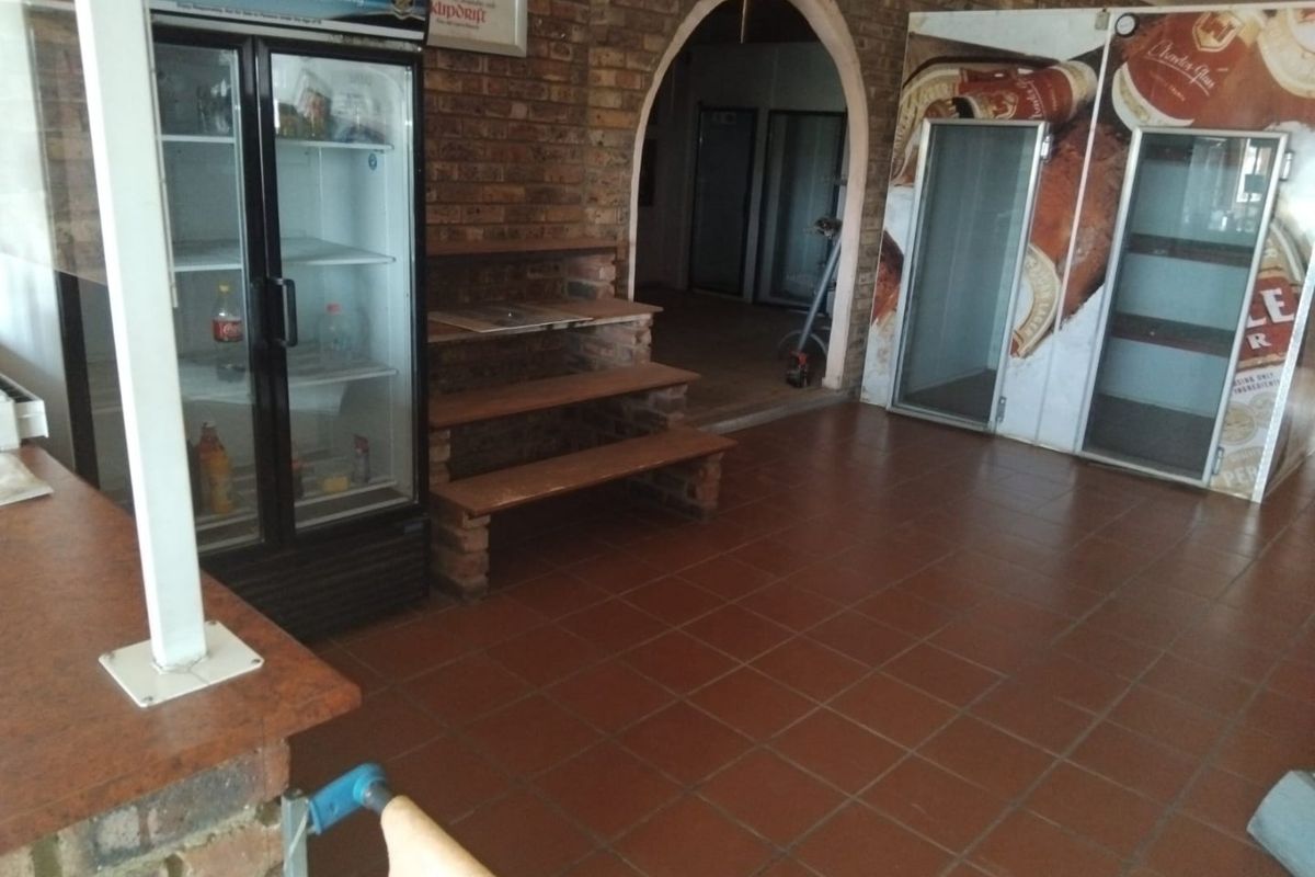 Commercial bar area featuring exposed brick walls, a distinctive arched entryway, tiled flooring, and built-in commercial refrigeration units.