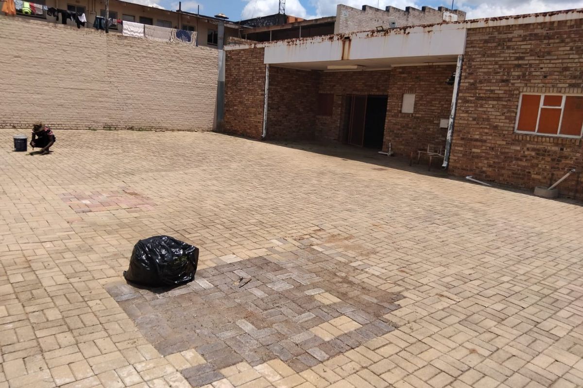 A paved rear courtyard area featuring brick wall construction, showing signs of wear and maintenance requirements on the facade and paving surfaces.