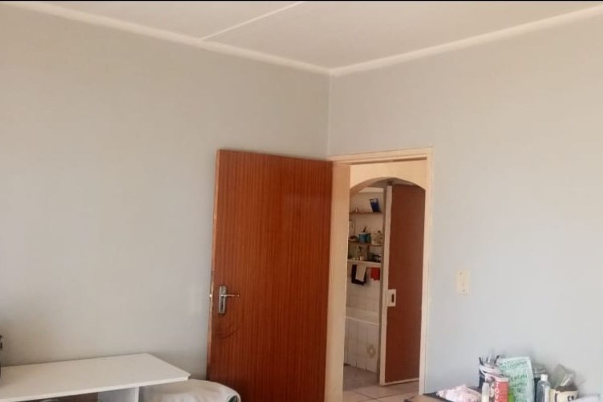 A simple, neutral-toned bedroom interior featuring a wooden door and access to an adjacent room.