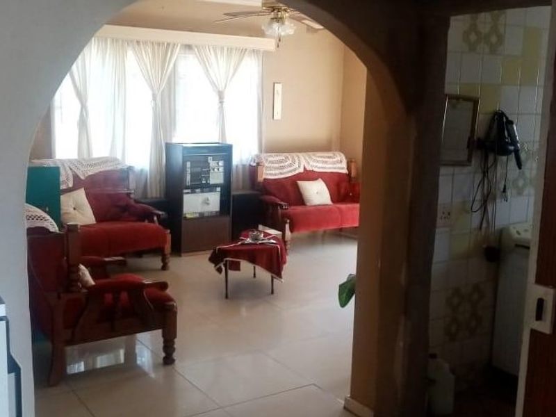 A living room area featuring tiled flooring and a distinctive arched entryway, connecting to adjacent spaces.