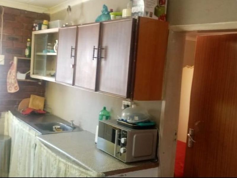 A compact kitchen area featuring laminate countertops, built-in cabinetry, and an exposed brick wall, requiring modernization to improve functionality and aesthetic appeal.