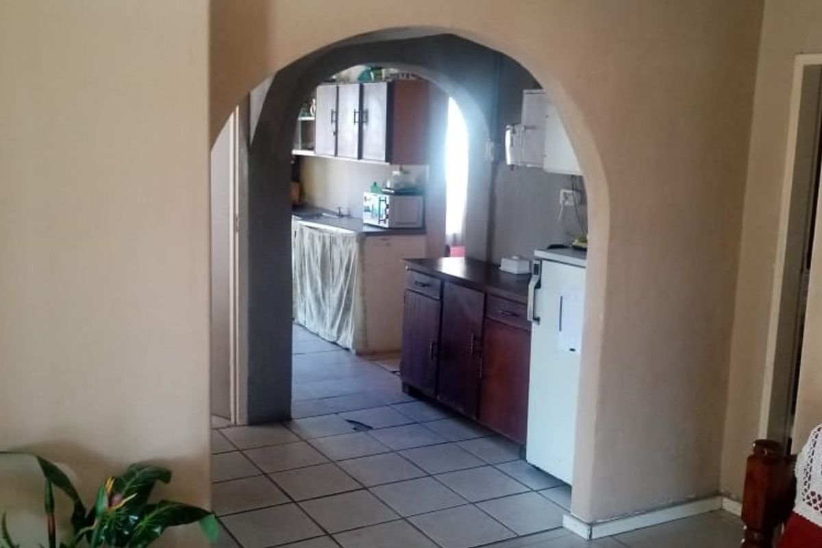 A view through an arched doorway into a functional kitchen featuring tiled flooring and built-in cabinetry.