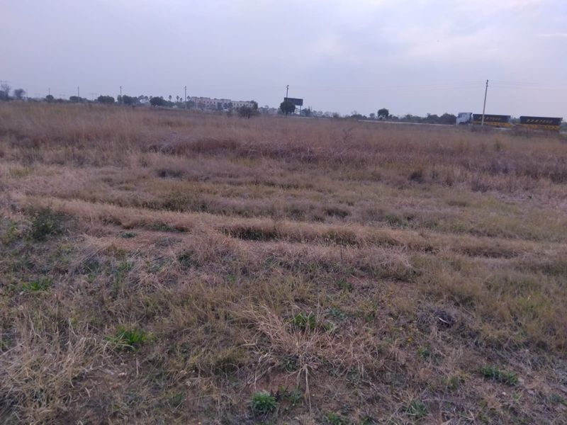 A wide-angle view of a vacant residential plot featuring open grassland and natural terrain.