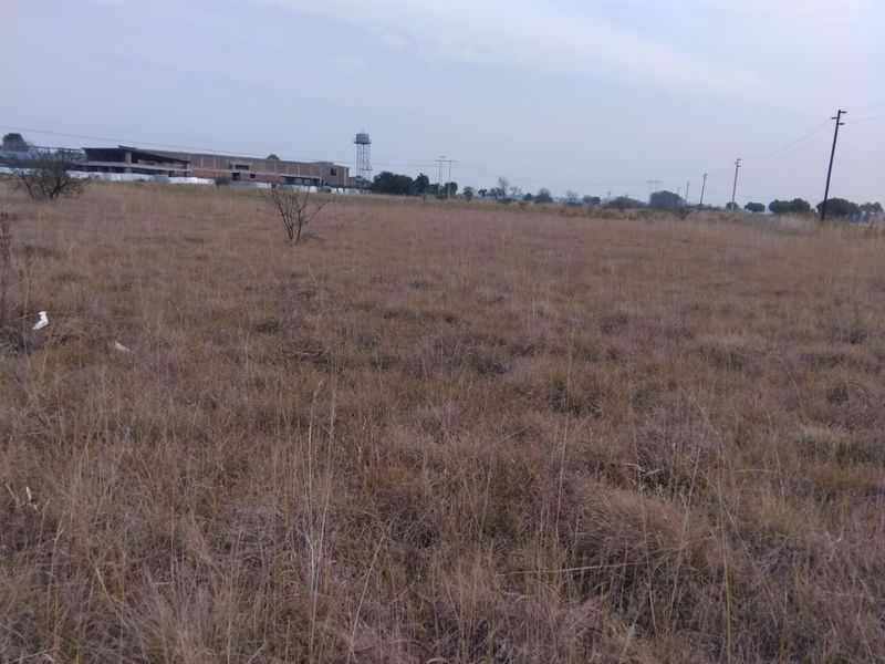 A wide, open vacant residential plot featuring dry grass, with distant views of a water tower and utility infrastructure.