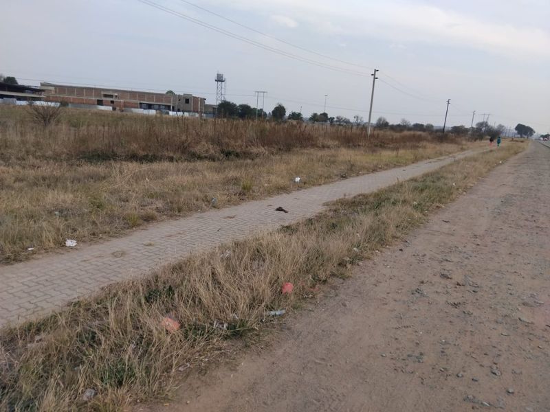 A view of the street frontage showing a paved walkway, utility infrastructure, and surrounding vacant land.
