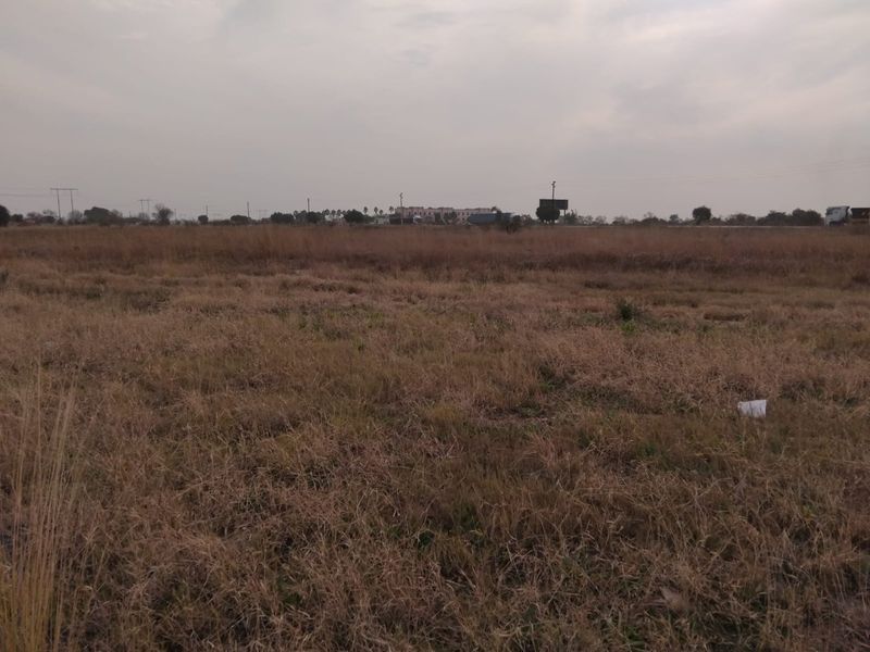 A wide, open expanse of vacant residential land featuring natural grassland under an overcast sky.