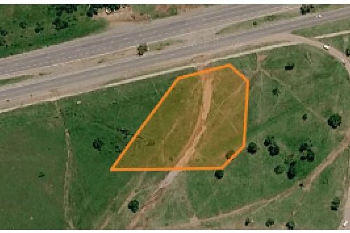 Aerial view of a vacant residential land plot with clear boundary markings, situated near major road infrastructure.