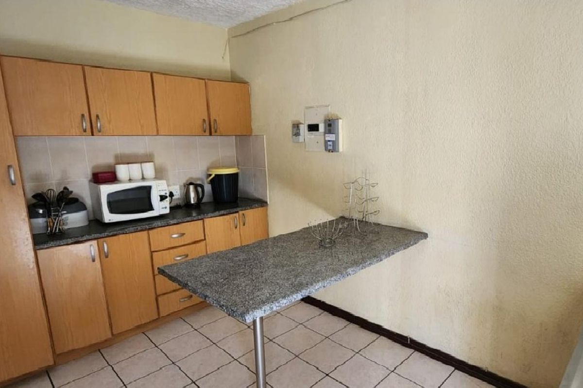 A compact kitchen featuring laminate cabinetry, tiled flooring, a tiled backsplash, and a functional breakfast bar extension.