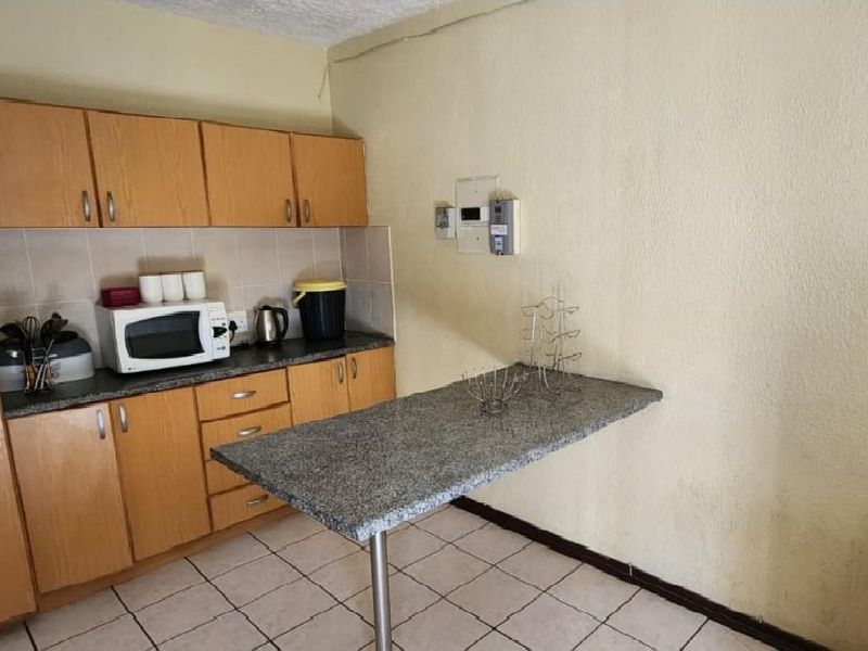 A compact kitchen featuring laminate cabinetry, tiled flooring, a tiled backsplash, and a functional breakfast bar extension.