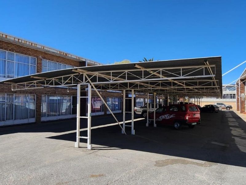 Outdoor parking area featuring a covered carport structure with metal roofing, situated between apartment building blocks with brick facades.