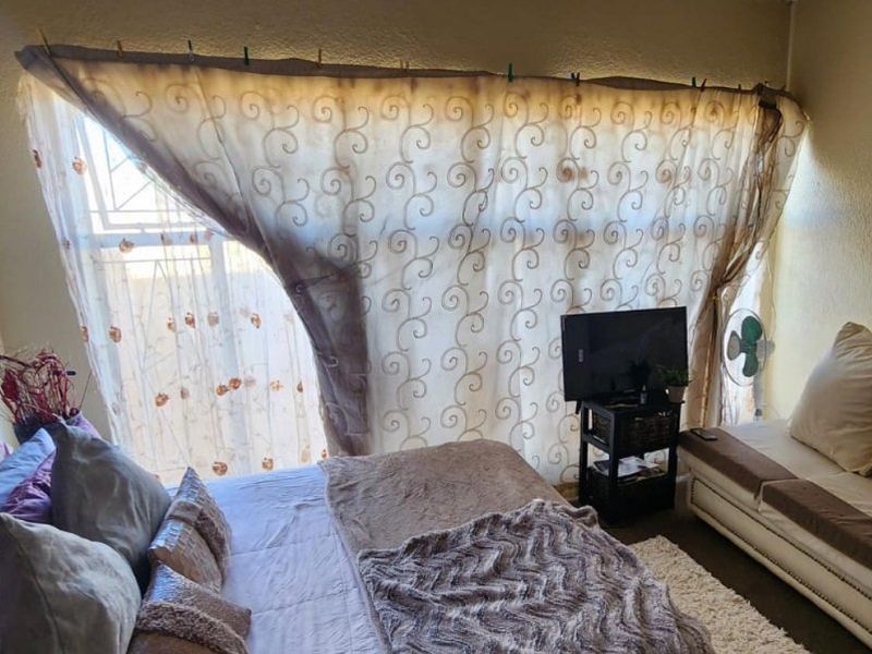 A bedroom featuring a large window with security gate, providing natural light and a functional layout for a comfortable living space.