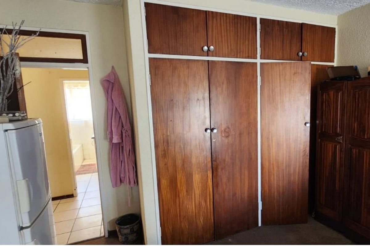 Bedroom featuring floor-to-ceiling built-in wooden cupboards with overhead storage, providing ample storage space with a dated aesthetic.
