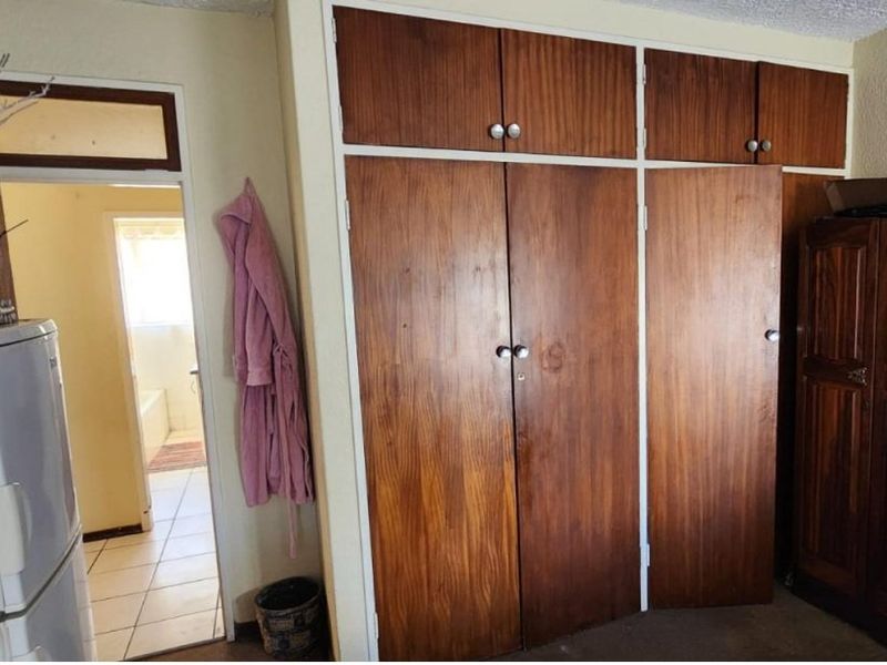 Bedroom featuring floor-to-ceiling built-in wooden cupboards with overhead storage, providing ample storage space with a dated aesthetic.