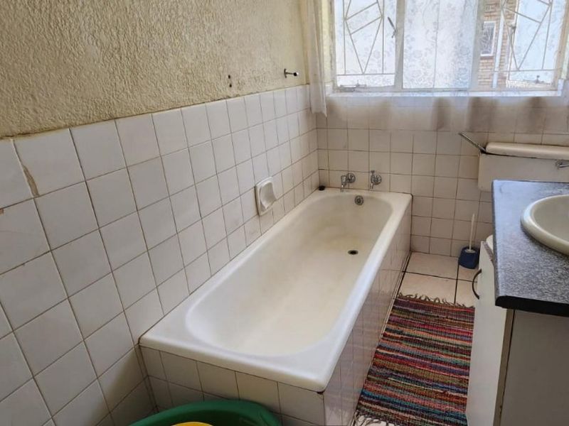 A dated bathroom featuring a bathtub, vanity basin, and tiled finishes, currently requiring maintenance and cosmetic updates to the wall surfaces.