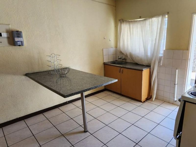 A compact kitchen featuring tiled flooring, a small sink area with base cabinetry, and a fixed breakfast counter.