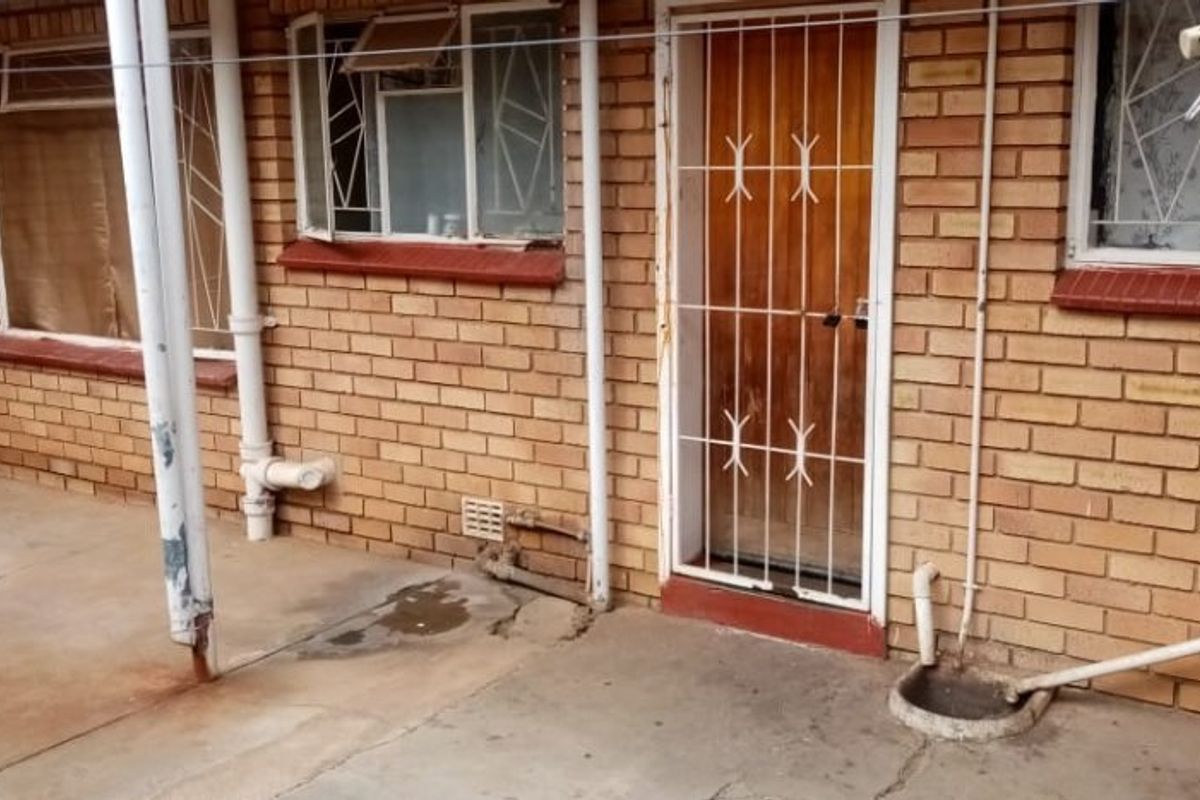 Rear exterior view of an apartment featuring a concrete patio, face brick walls, and security gates on the windows and door.