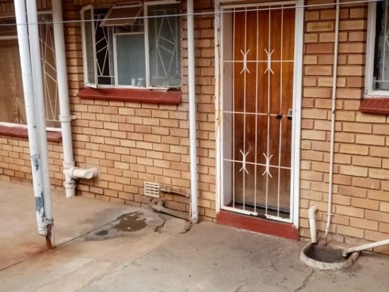 Rear exterior view of an apartment featuring a concrete patio, face brick walls, and security gates on the windows and door.