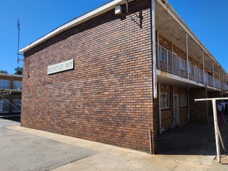 Exterior view of a multi-story apartment building featuring face brick construction, open-air walkways with metal railings, and an adjacent asphalt parking area.
