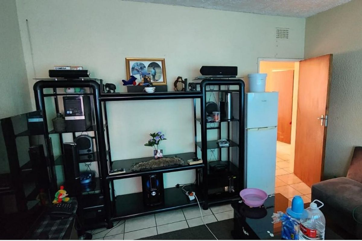 A living room area featuring tiled flooring and a ventilation grille, currently occupied by personal storage units and furniture.