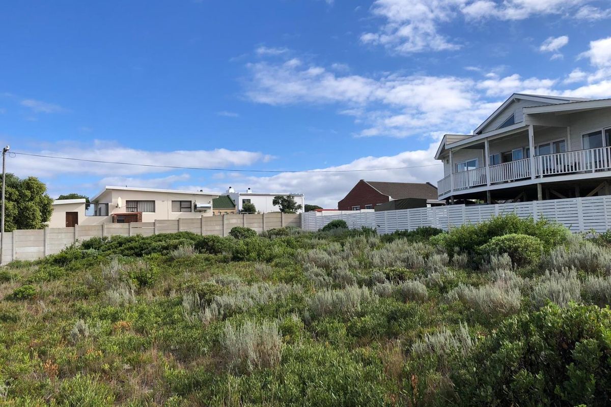 A vacant residential plot featuring natural coastal vegetation, enclosed by a precast concrete boundary wall and a white timber fence.
