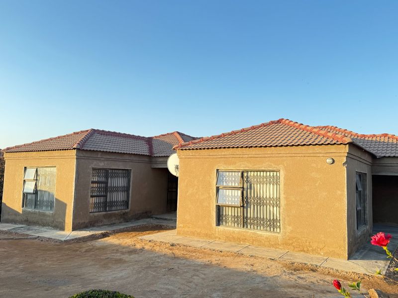Front elevation of a single-story house featuring a tiled roof, security gates on windows, and unfinished exterior wall plastering.