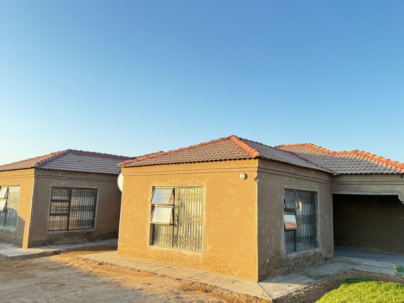 Front elevation of a single-story house featuring plastered walls, tiled roofing, and security-fitted windows with a paved walkway.