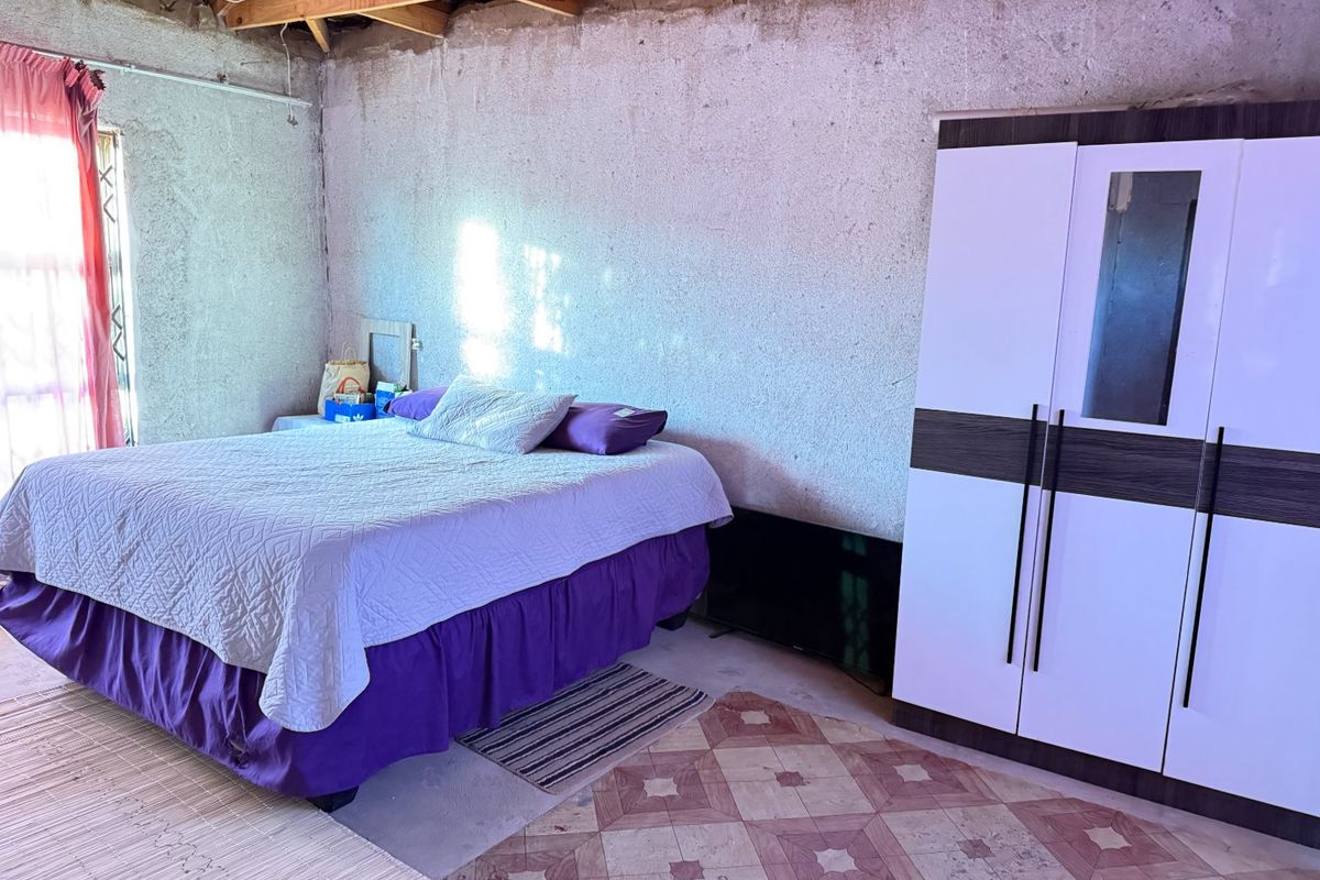 A bedroom featuring exposed timber roof trusses, unfinished textured concrete walls, and patterned floor tiles, offering a rustic space ready for renovation.