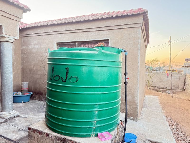 Exterior view of the rear property area featuring a large green water storage tank mounted on a concrete plinth.