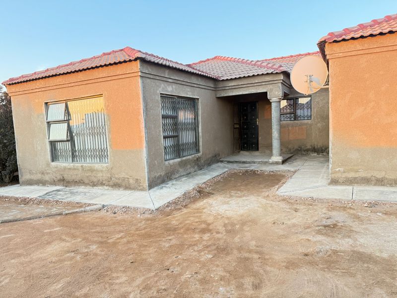 Front view of a single-story house featuring a tiled roof, security gates, and an unfinished exterior facade with a paved entrance area.