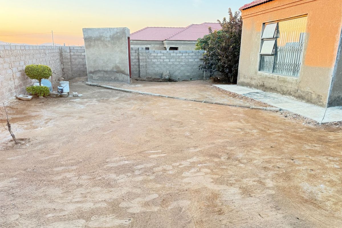 A spacious rear yard featuring concrete block boundary walls, security features on the window, and an unfinished exterior wall finish.