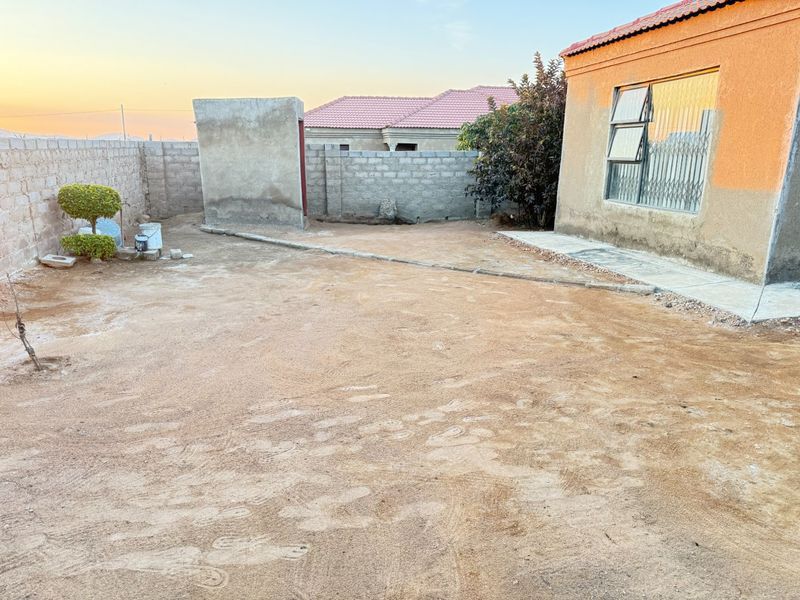 A spacious rear yard featuring concrete block boundary walls, security features on the window, and an unfinished exterior wall finish.