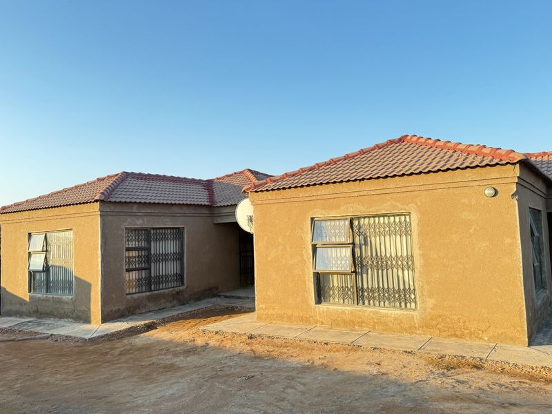 Front elevation of a single-story house featuring a tiled roof, plastered exterior walls, and security-fitted windows with a paved walkway.