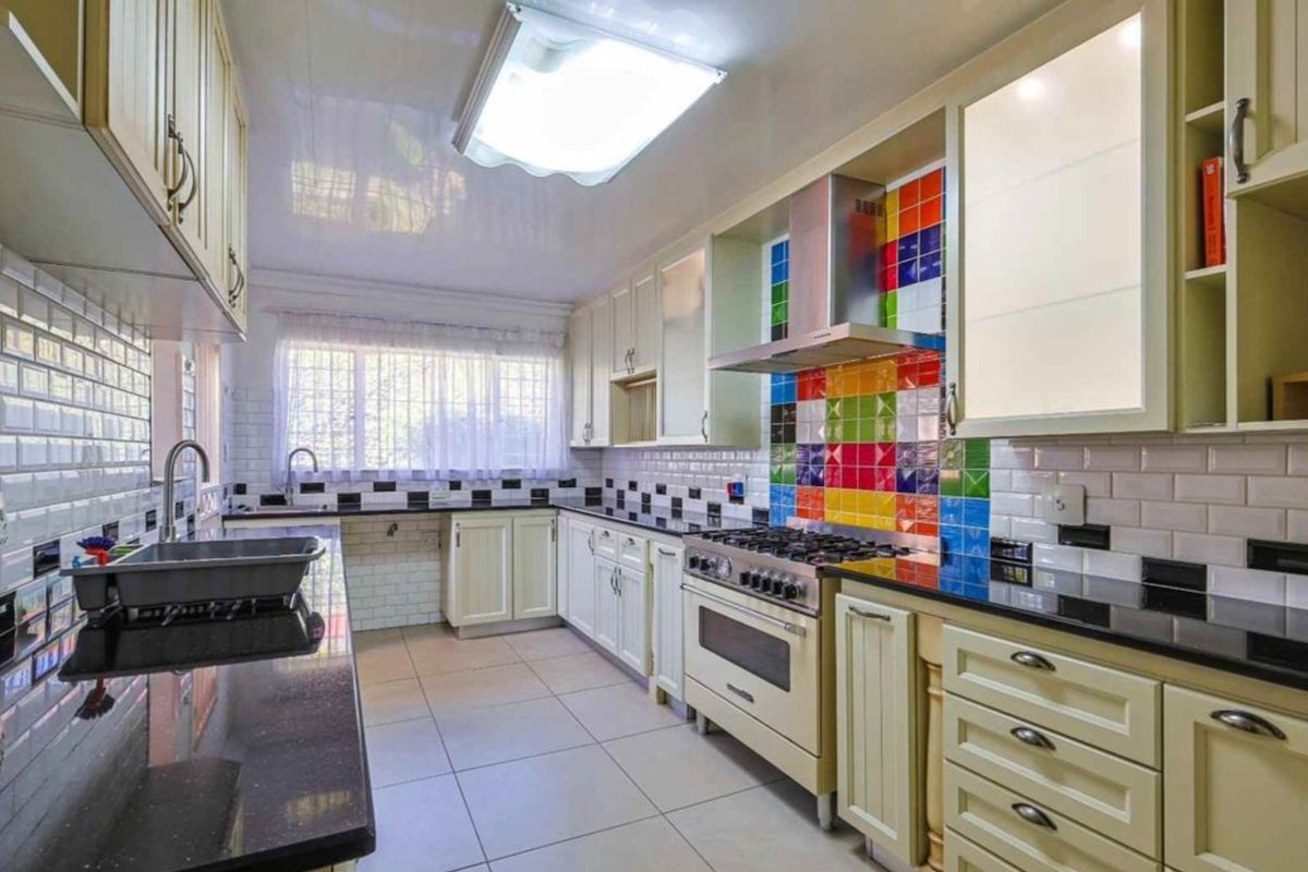 A functional kitchen featuring cream cabinetry, granite countertops, a gas stove with extractor fan, and a colorful tiled backsplash.