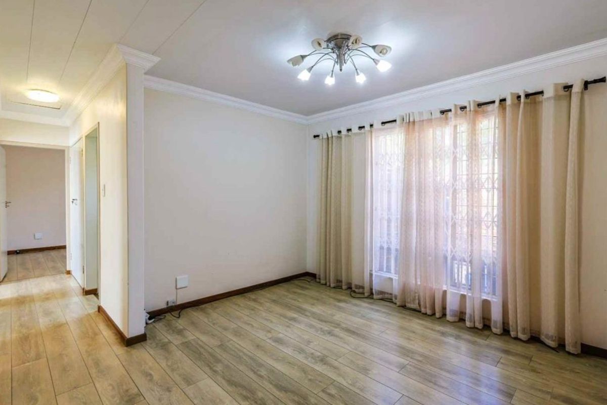 A bright, empty living room featuring wood-look laminate flooring, crown molding, and a large window with security gate access.
