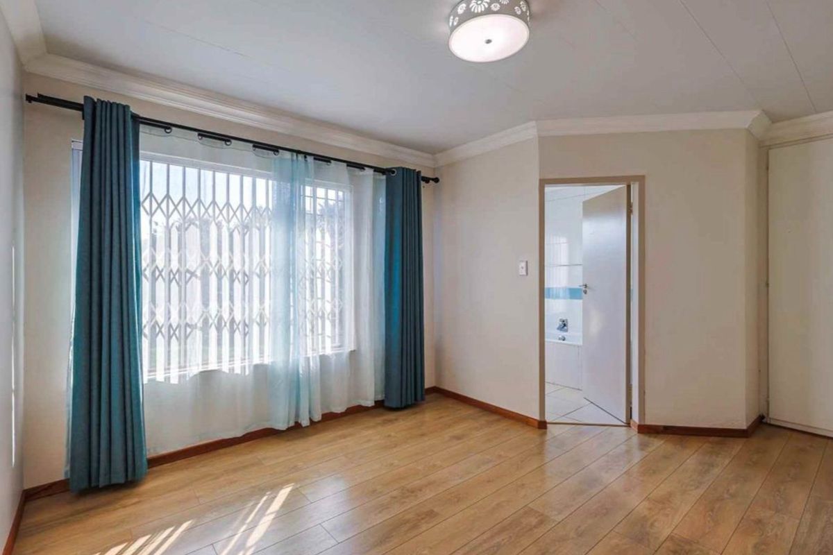 A bright, empty bedroom featuring laminate flooring, a security gate on the window, and direct access to an en-suite bathroom.