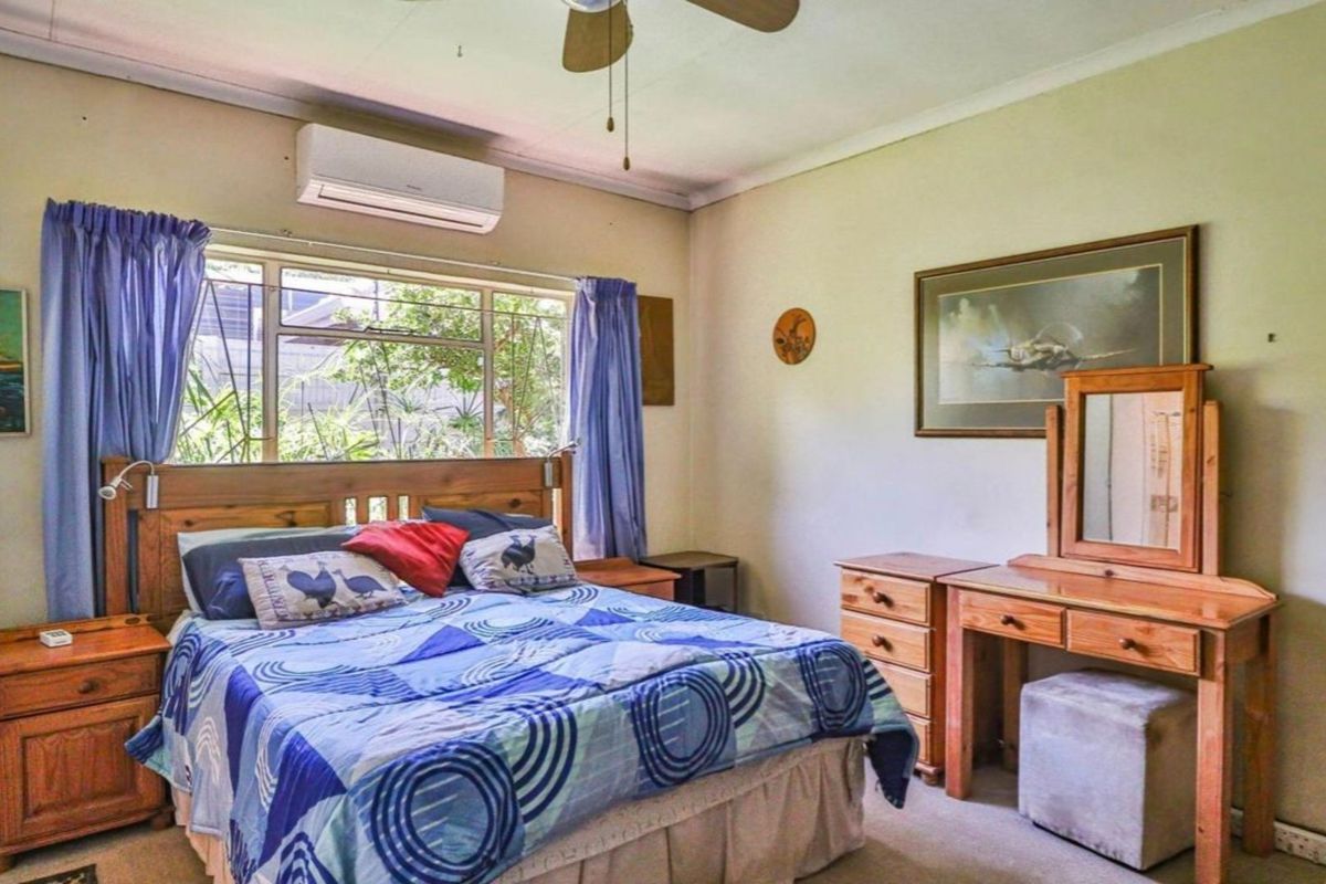 A functional bedroom featuring a ceiling fan, wall-mounted air conditioning unit, and large window providing natural light.