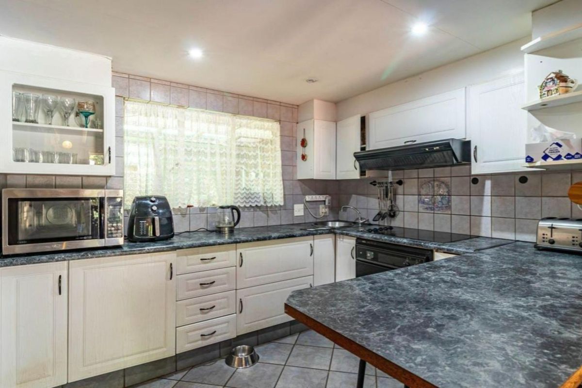 A functional kitchen featuring white cabinetry, dark laminate countertops, tiled backsplash, and integrated appliances including an oven, hob, and extractor fan.